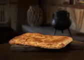 Empanada grande de obrador, dorada y recién horneada, sobre una tabla de madera